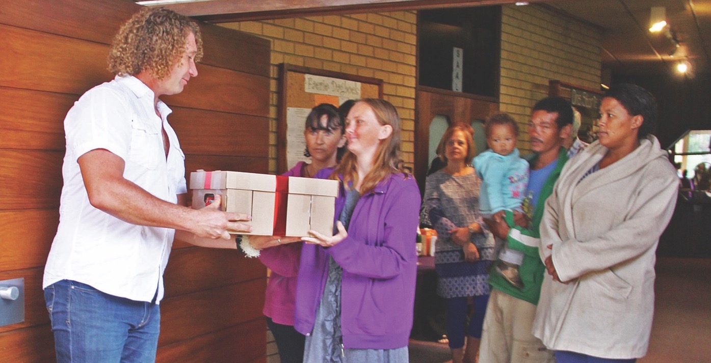 Die sanger Ghapi gee ’n kospakkie weg by die bekendstelling van die Christelike Maatskaplike Raad van Gauteng-Oos se Pasella Pakkie-voedselprojek. Dit is die vaandel waaronder die 13 CMR-kantore in die streek hulle voedselprojekte voortaan gaan bedryf. Die verskillende takke se projekte verskil van mekaar. So vra die CMR van Lyttelton-Oos vir lidmate om Sondag met middagete ’n ekstra bord kos te skep, dit te vries en dit vir hulle te bring. Dié kos word dan in die week uitgedeel. Ander kantore versprei weer net nie-bederfbare kos. Almal is egter afhanklik van skenkings. Enigeen wat ’n bydrae wil maak, kan vir Sandra Kruger by 012 361 4613/19 skakel. Sy sal kan sê waar en hoe mense kan help. Foto: Ilse Ferreira